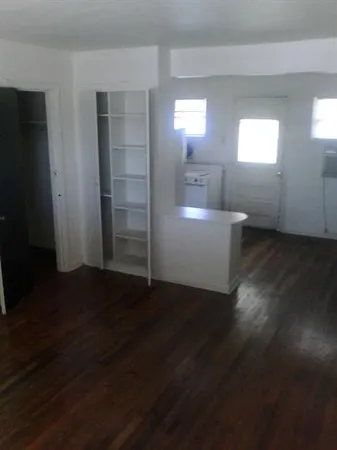 an empty room with wooden floor cabinet and windows