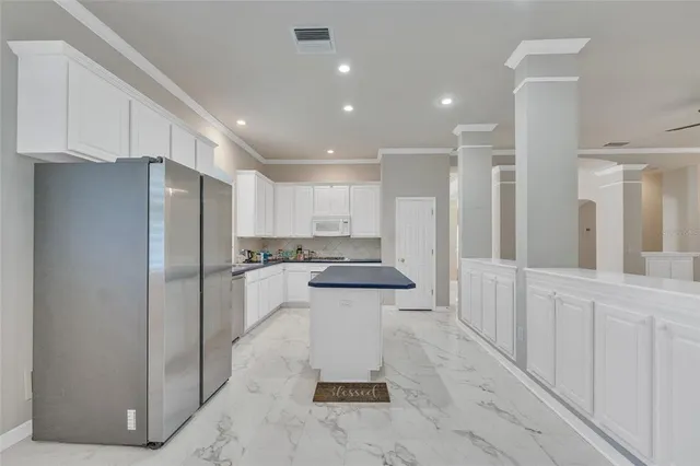 a kitchen with stainless steel appliances granite countertop a sink dishwasher a refrigerator and white cabinets with wooden floor