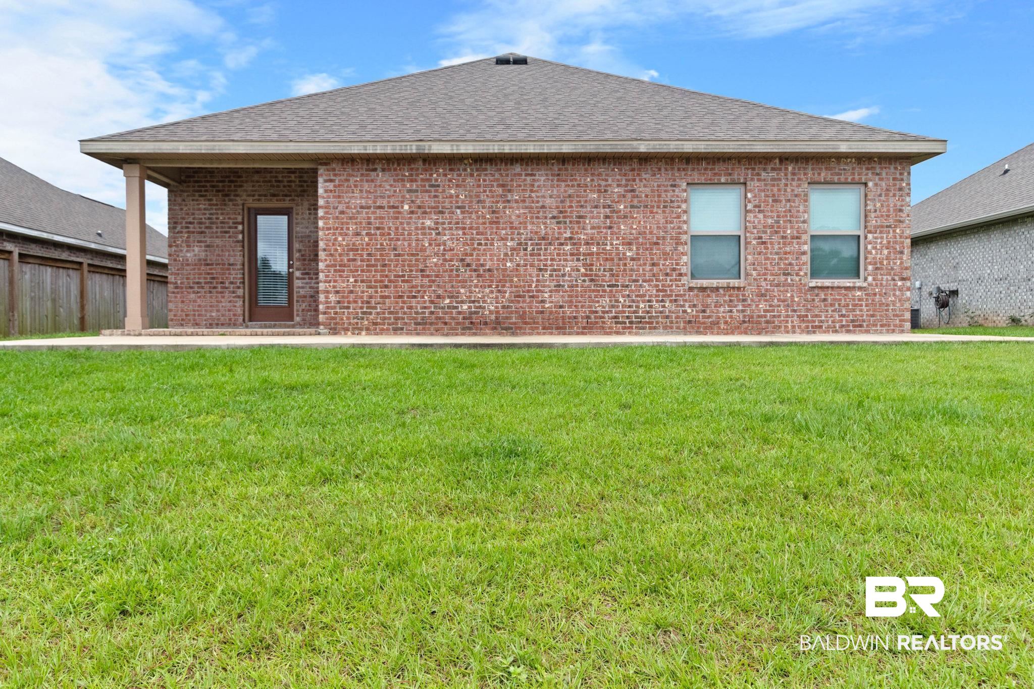 1710 Grouse Street Foley, AL 36535 - Photo 61 of 76 Brick exterior with a gabled roofline, concrete patio, covered porch area with a column, and a rear entry door with integrated glass