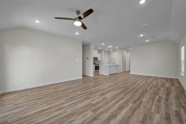 a view of an empty room with wooden floor and a ceiling fan