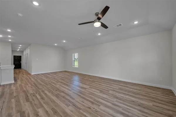 an empty room with wooden floor fan and windows