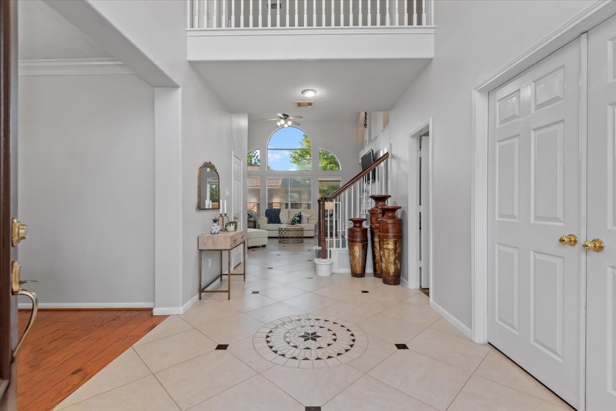 6507 Quiet Pointe Drive Spring, TX 77389 - Photo 19 of 46 This photo showcases a bright, open entryway with elegant tile flooring and a decorative medallion. A staircase with wooden accents leads to the upper level, while large windows fill the space with natural light. The area features tasteful decor and a glimpse of a cozy living room beyond.