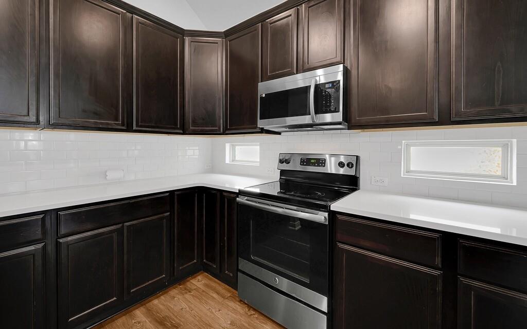 2720 Beutel Road Lorena, TX 76655 - Photo 12 of 37 Kitchen with stainless steel appliances, dark brown cabinets, light wood-style floors, decorative backsplash, and light stone counters