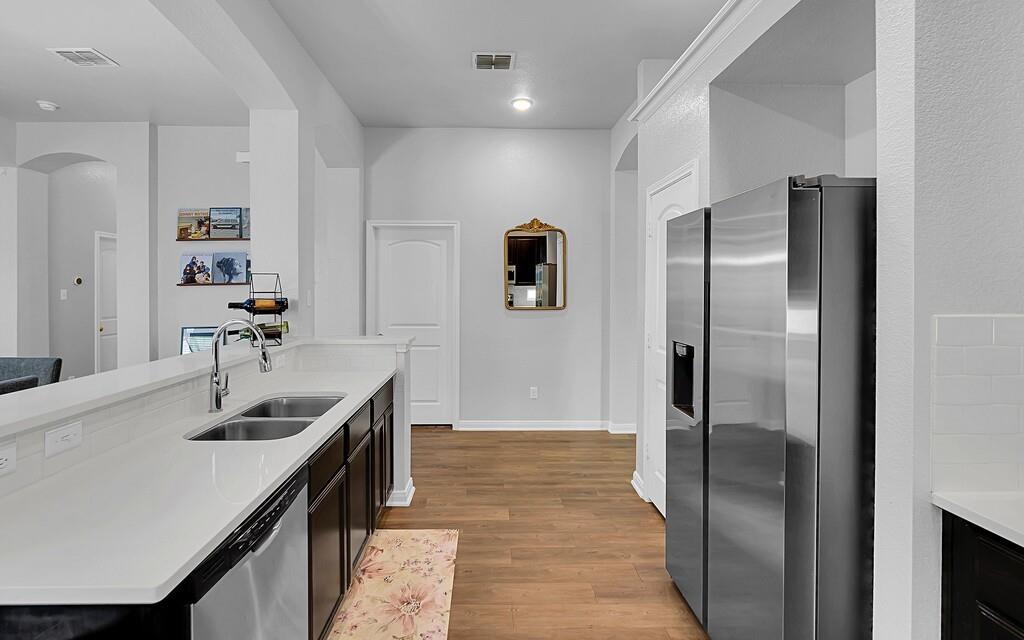 2720 Beutel Road Lorena, TX 76655 - Photo 13 of 37 Kitchen featuring appliances with stainless steel finishes, arched walkways, light wood finished floors, light stone countertops, and dark cabinets
