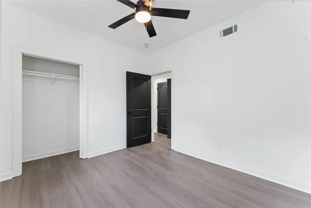 an empty room with wooden floor ceiling fan and windows