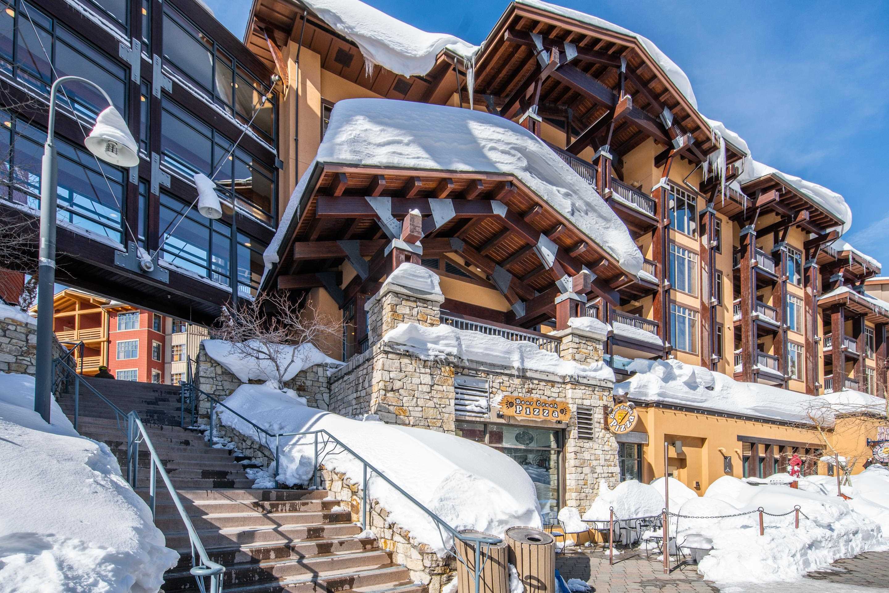 6201 Minaret Road, Unit 2221 Mammoth Lakes, CA 93546 - Photo 42 of 44 Multi-story building featuring warm yellow stucco, exposed timber framing, stone accents, and snow-covered balconies