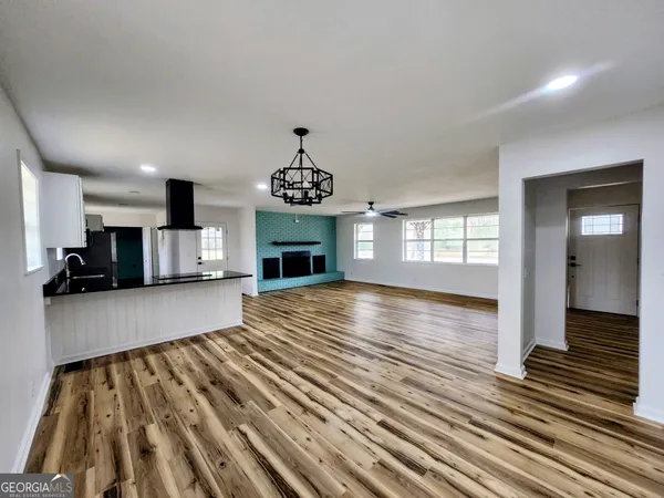 a view of an empty room and kitchen with wooden floor