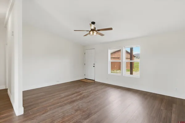 an empty room with wooden floor ceiling fan and windows