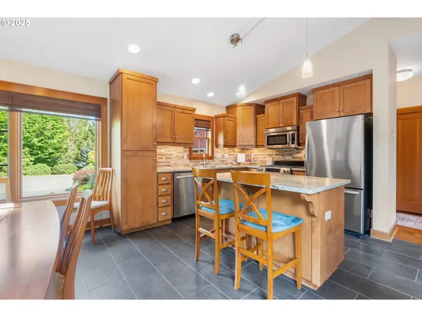 a kitchen with stainless steel appliances a dining table chairs refrigerator and microwave