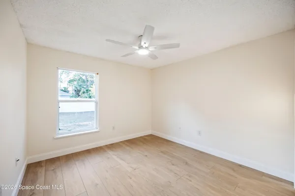 an empty room with wooden floor ceiling fan and windows
