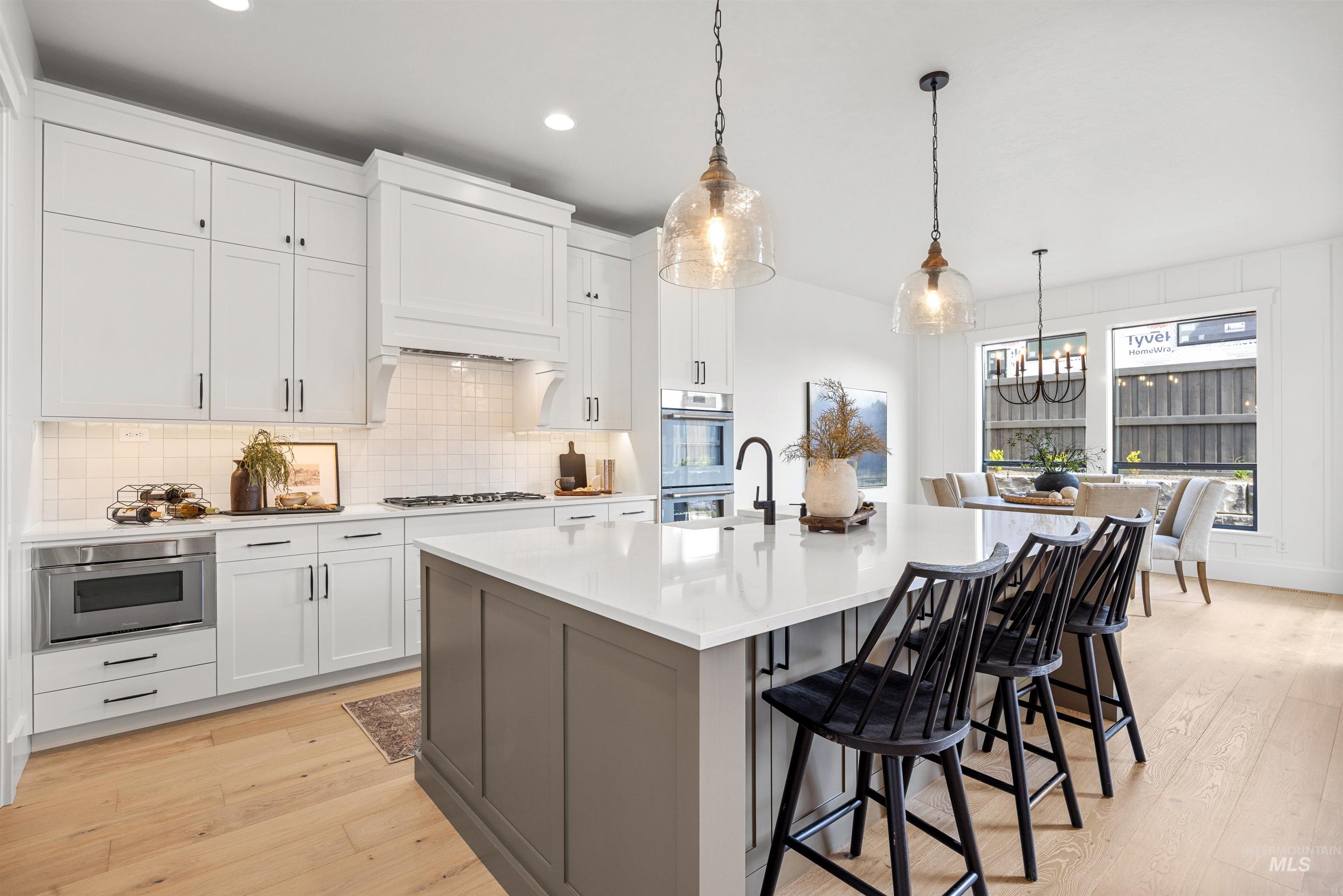 5940 South Pinpoint Way Meridian, ID 83642 - Photo 22 of 40 Light wood-finish flooring with white cabinetry, a built-in microwave drawer, and a large central island featuring a sink and pendant lighting
