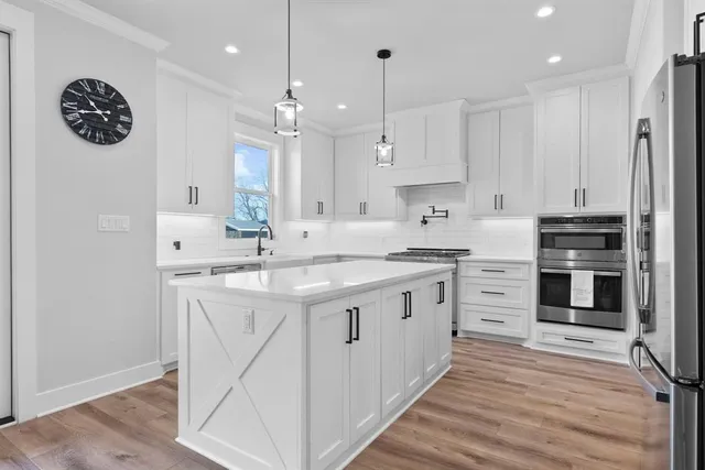 a kitchen with stainless steel appliances granite countertop a sink a stove a refrigerator and white cabinets with wooden floor