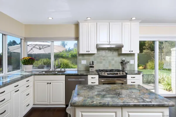 a kitchen with kitchen island granite countertop a stove a sink and white cabinets