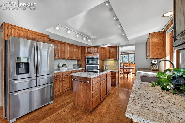 a kitchen with stainless steel appliances granite countertop a stove top oven a refrigerator a dining table and chairs with wooden floor