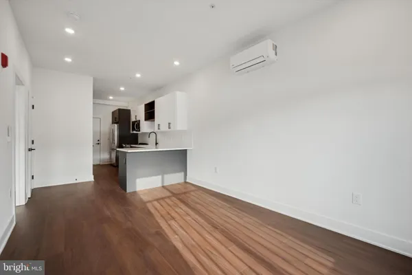 a view of an empty room with wooden floor and a kitchen