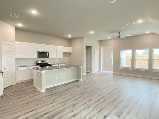 a view of kitchen with kitchen island stainless steel appliances refrigerator stove and wooden floor