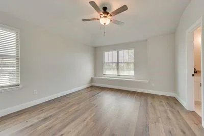 an empty room with wooden floor chandelier fan and windows
