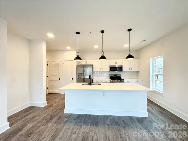 a large kitchen with stainless steel appliances a large counter top a stove a chimney a large window and wooden floor