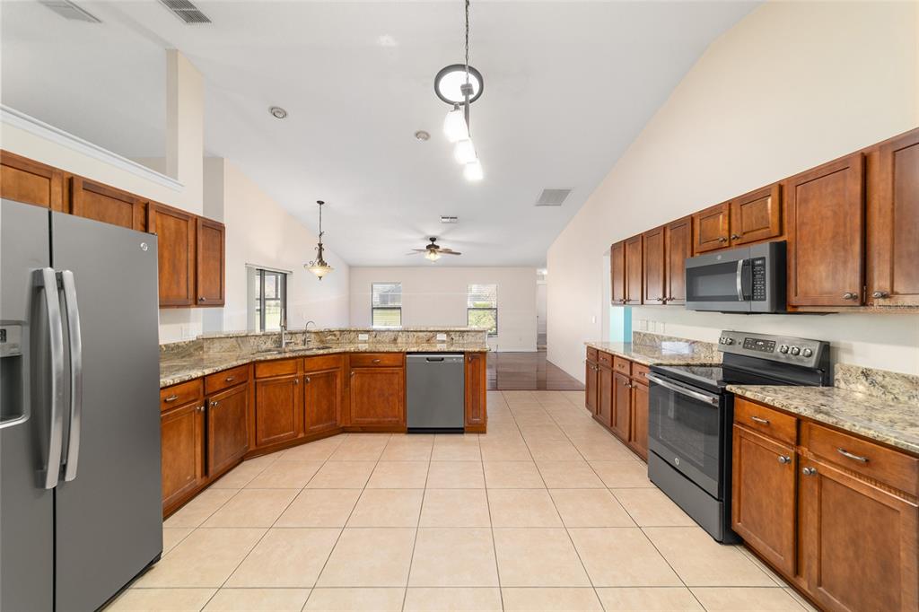 4037 Southeast 40th Street Ocala, FL 34480 - Photo 19 of 38 a large kitchen with stainless steel appliances granite countertop a stove top oven a sink dishwasher a dining table and chairs with wooden floor