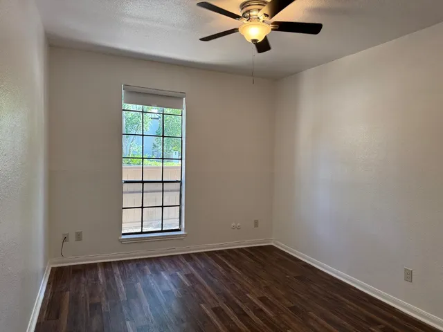 an empty room with wooden floor fan and windows