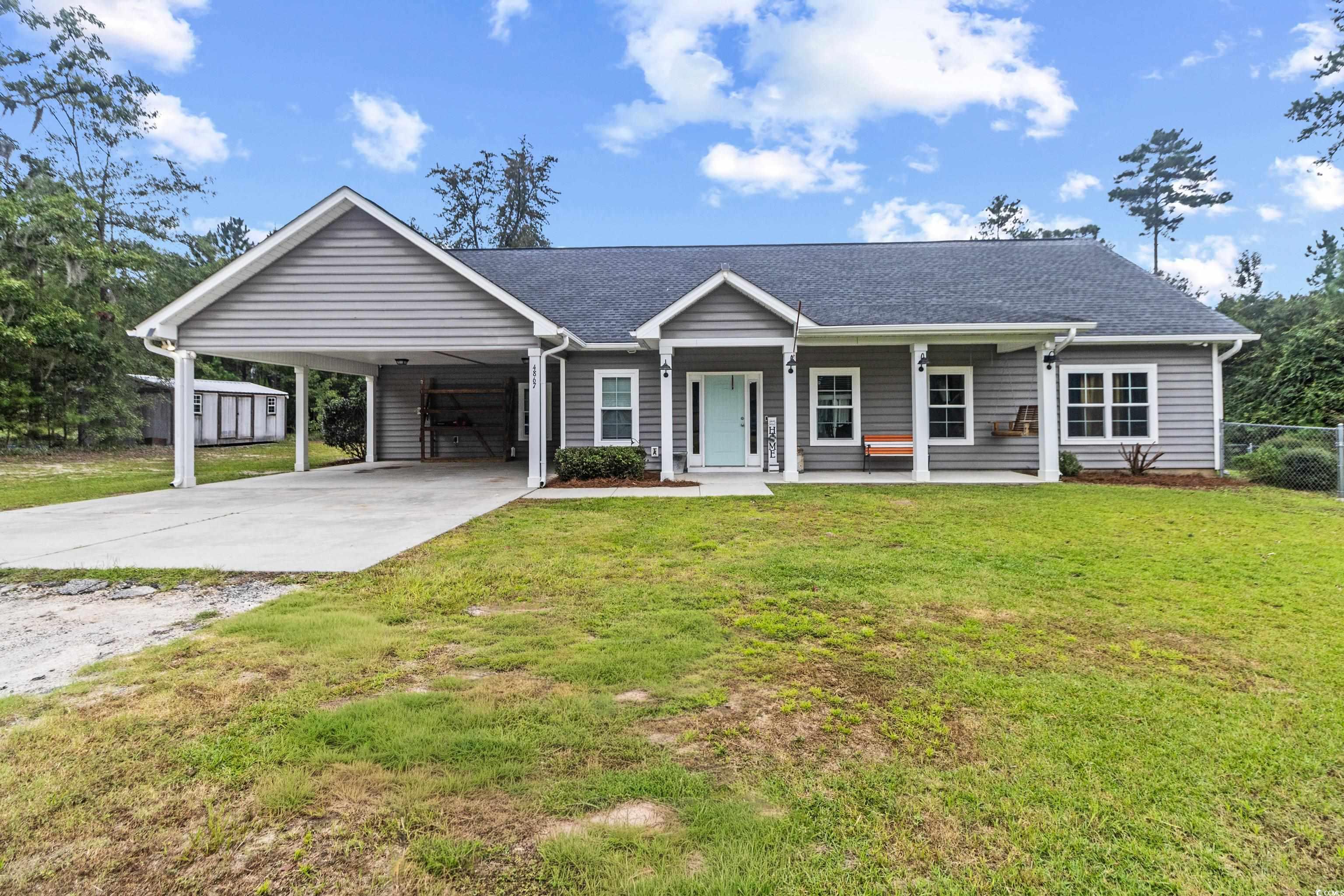 Ranch-style house with a carport, driveway, a shingled roof, covered porch, and a front lawn
