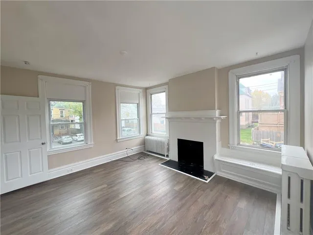 an empty room with wooden floor fireplace and windows