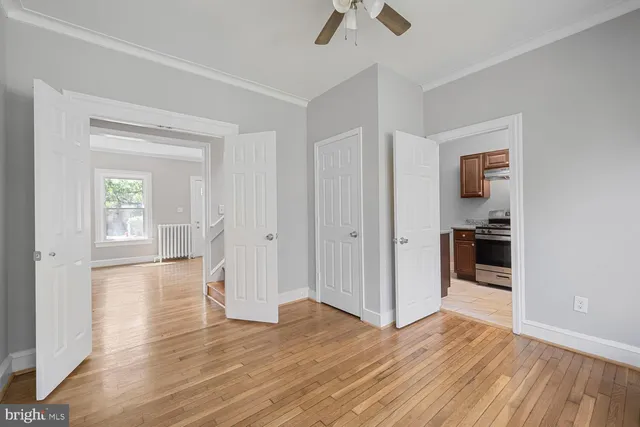 an empty room with wooden floor and way to kitchen