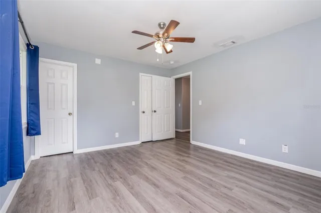 a view of an empty room with wooden floor and a ceiling fan
