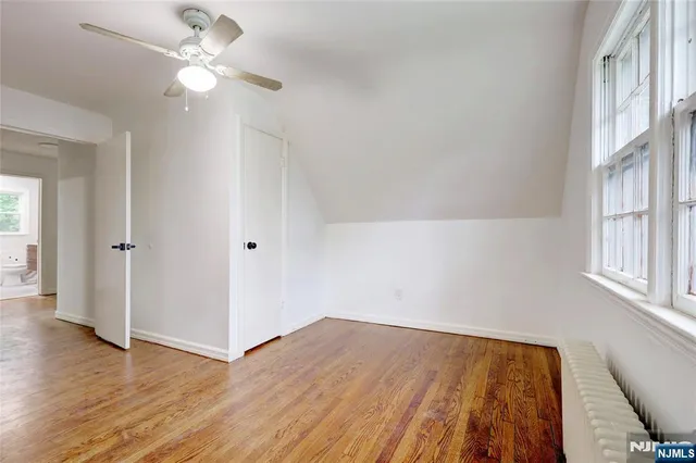 an empty room with wooden floor chandelier fan and windows