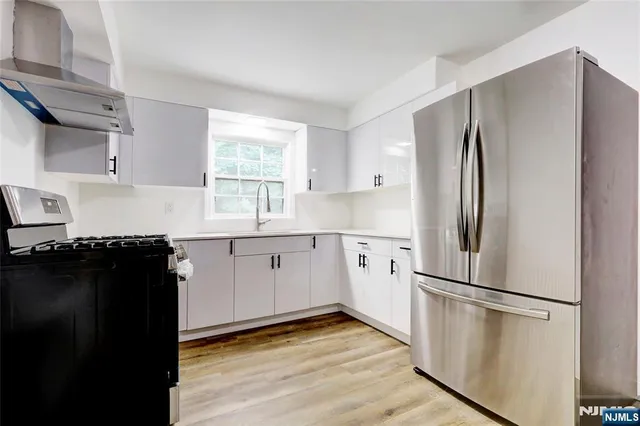 a kitchen with a refrigerator a stove a sink and white cabinets with wooden floor