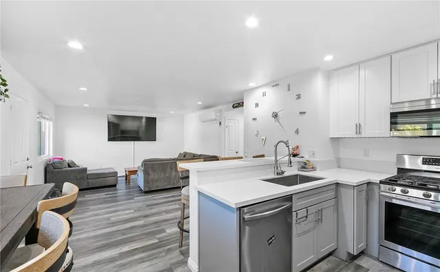 a kitchen with stainless steel appliances a stove a sink a refrigerator white cabinets and couches with wooden floor