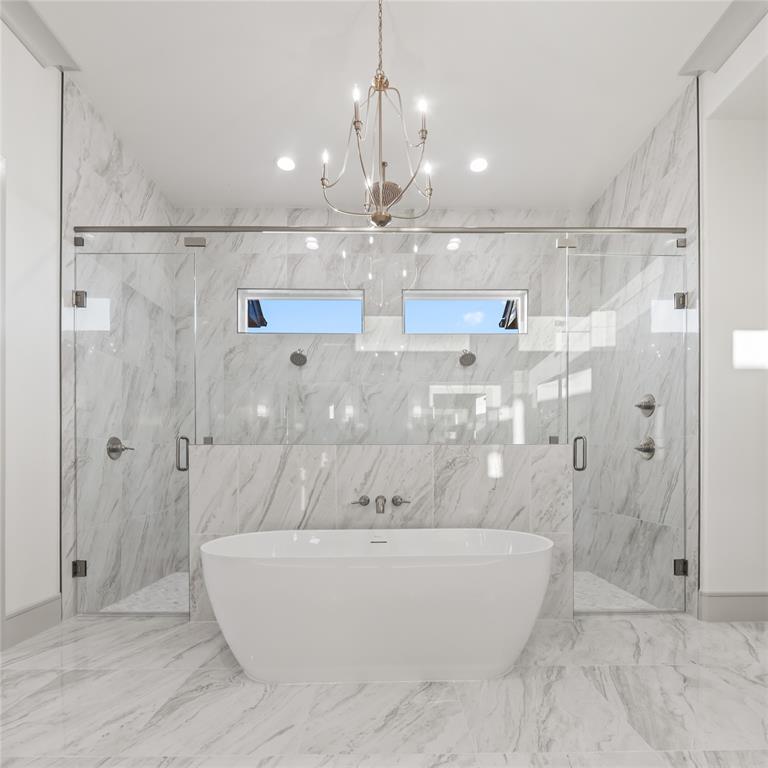 724 Cooper Trail Weatherford, TX 76087 - Photo 28 of 37 Freestanding soaking tub centered in a spacious bathroom featuring floor-to-ceiling marbled tile, dual glass-enclosed showers, and a chandelier