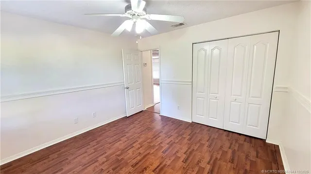 an empty room with wooden floor closet fan and windows