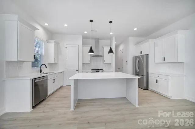 a large white kitchen with a stove a sink dishwasher and a refrigerator with wooden floor