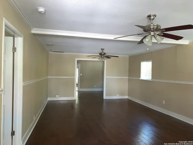 an empty room with wooden floor fan and windows