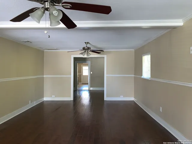 an empty room with wooden floor chandelier fan and windows