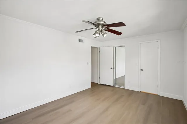 an empty room with wooden floor ceiling fan and windows