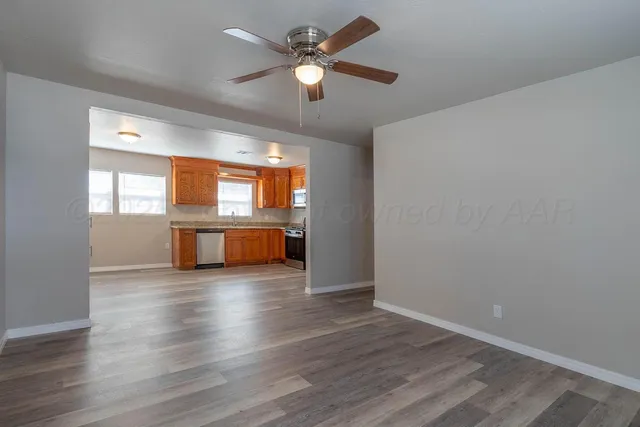an empty room with wooden floor chandelier fan and windows