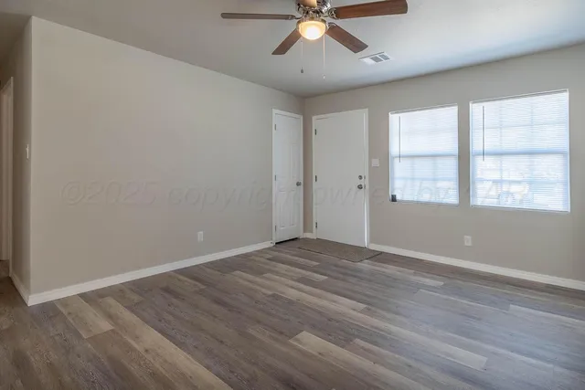 an empty room with wooden floor fan and windows