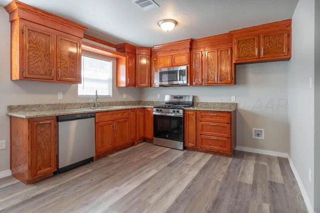 a kitchen with stainless steel appliances granite countertop wooden cabinets a sink and dishwasher with wooden floor