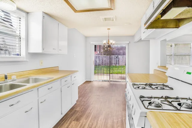 a open kitchen with granite countertop a stove sink and white cabinets with wooden floor