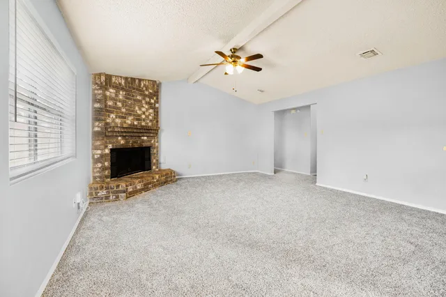 a view of an empty room with chandelier fan and fire place