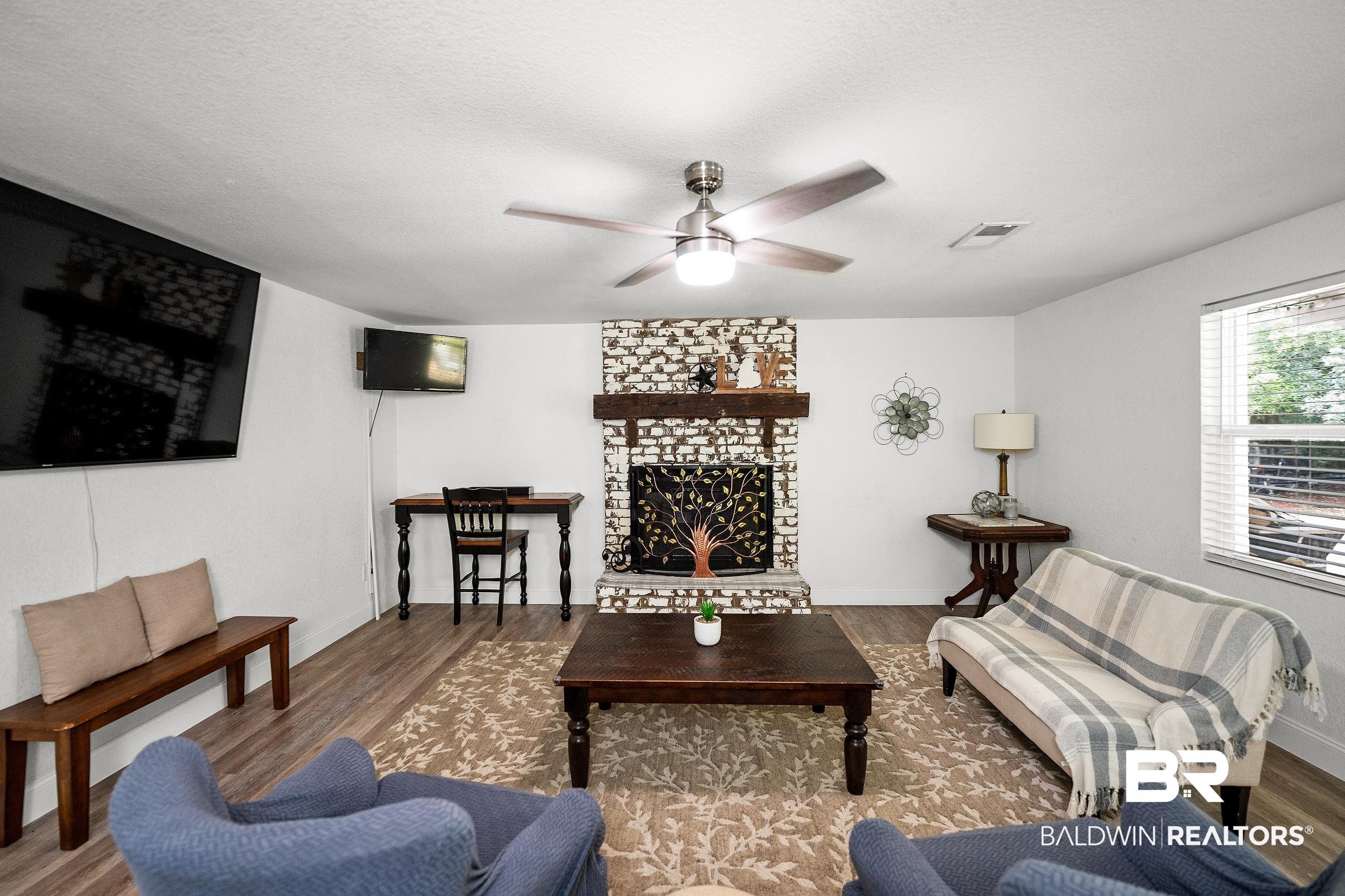 33129 Antietam Road Lillian, AL 36549 - Photo 3 of 31 Living area featuring wood-finish flooring, a white brick fireplace with a wood mantel, and a ceiling fan with integrated lighting