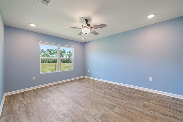 an empty room with wooden floor fan and windows