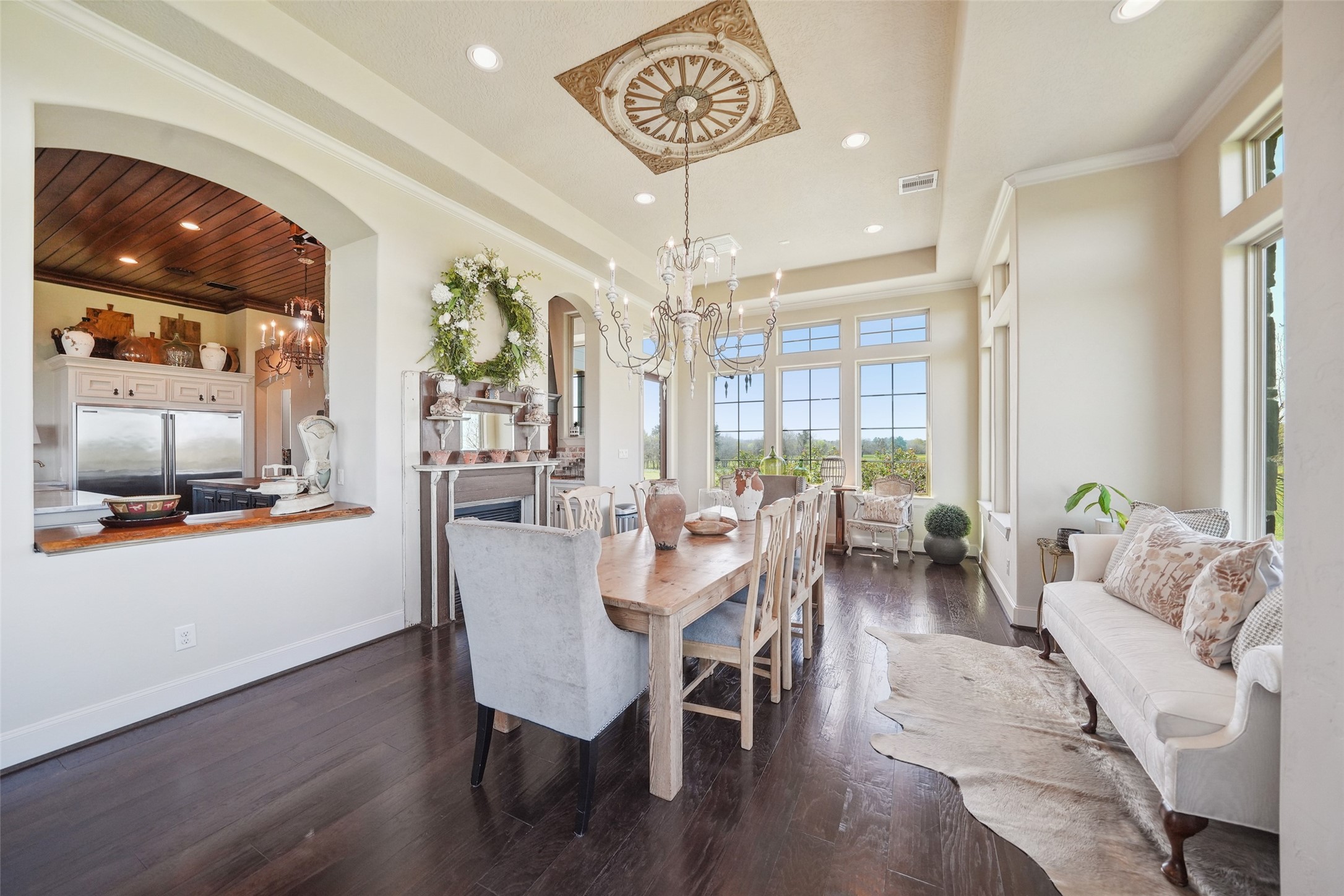 460 Bishop Road Huntsville, TX 77320 - Photo 15 of 50 The breakfast room showcases an elegant dining space bathed in natural light from three walls of expansive windows, perfectly framing breathtaking views and stunning sunsets complemented by a vintage-inspired chandelier hanging from an intricately designed ceiling medallion with a double-sided fireplace shared with the kitchen.
