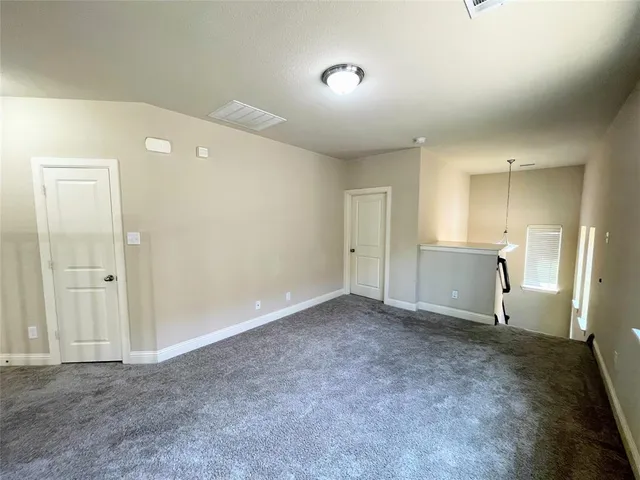 a view of an empty room with wooden floor kitchen view and a window