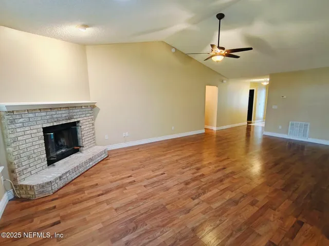 a view of an empty room with wooden floor a fireplace and a window