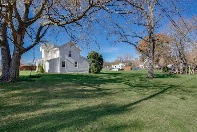 a view of a white house with a big yard and large tree