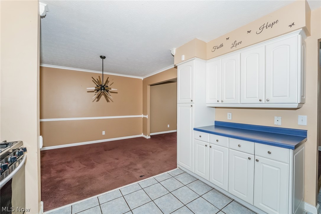 215 Randel Avenue Akron, OH 44313 - Photo 7 of 20 Kitchen with stove, light carpet, hanging light fixtures, white cabinetry, and ornamental molding