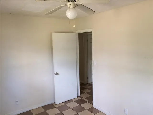 an empty room with a chandelier fan and wooden floor